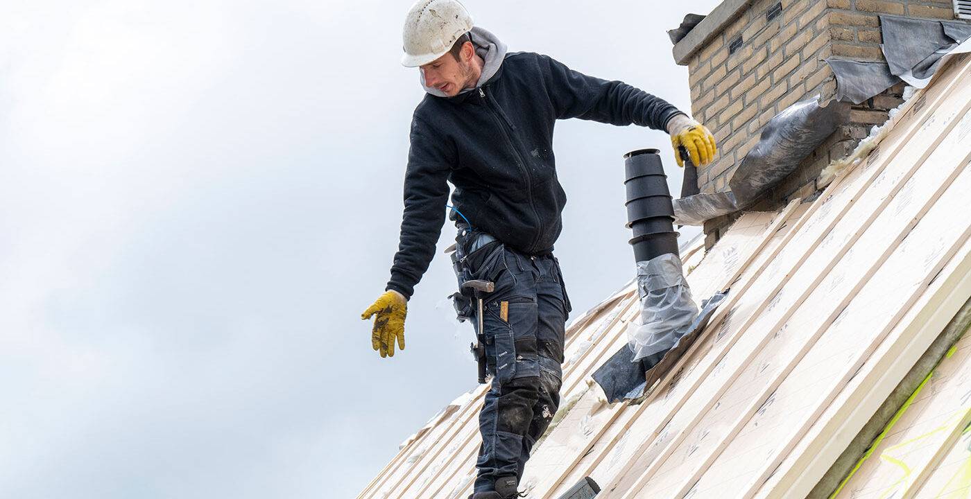 Roofer on a steep roof handing shingles to other worker